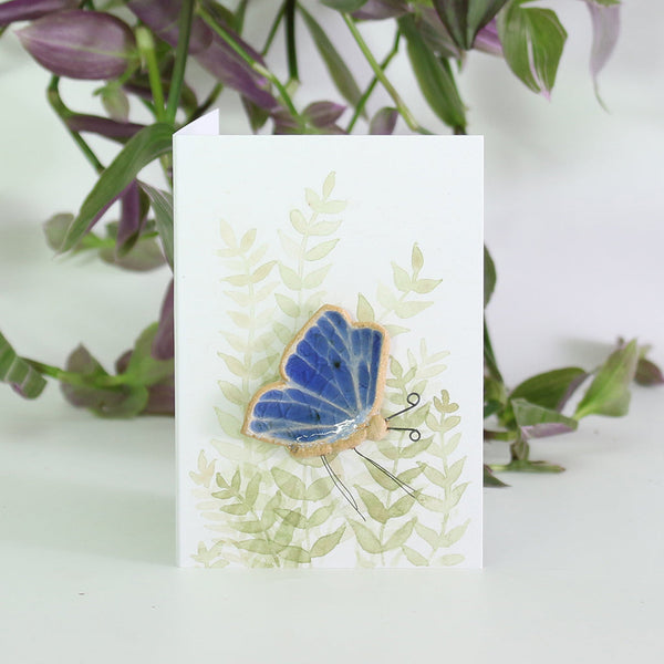 small ceramic and glass sapphire blue butterfly plant decoration on gift card with watercolour leaves