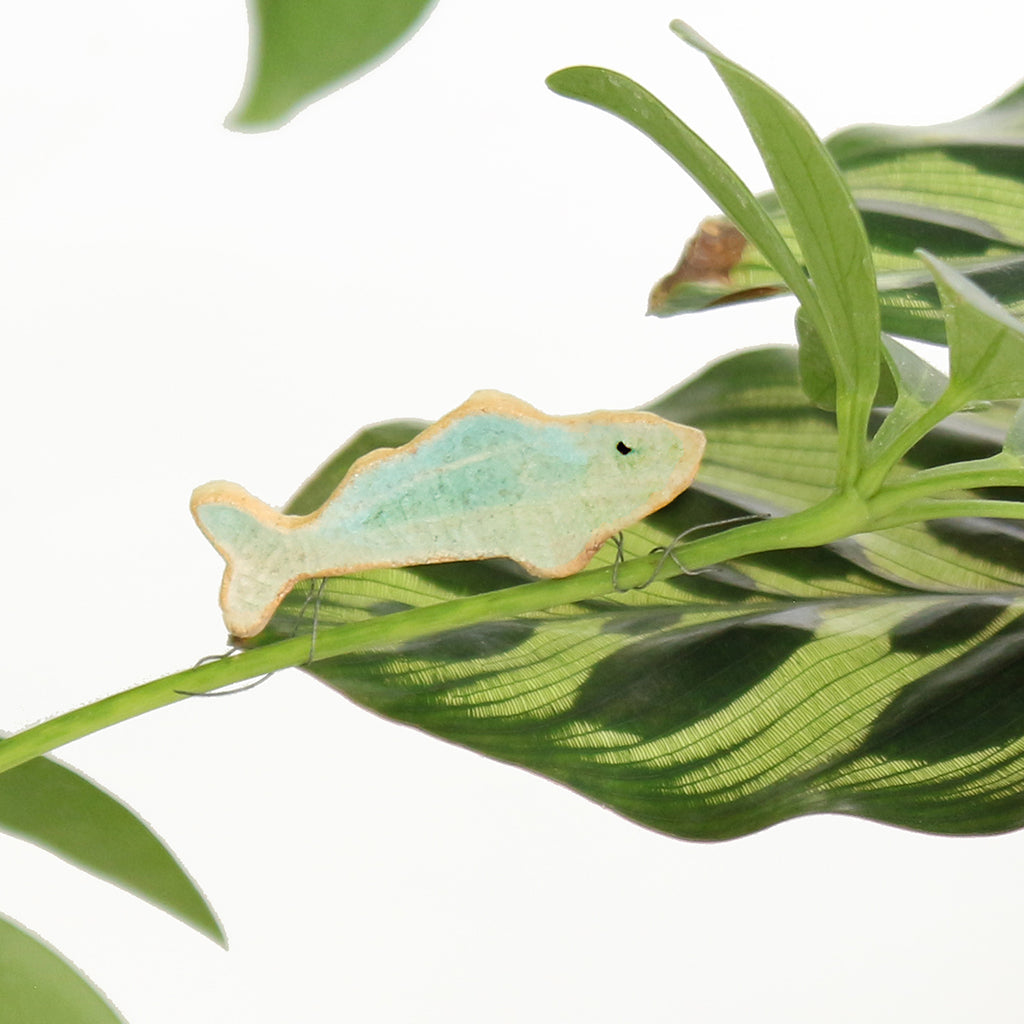 small ceramic and glass aqua blue fish plant decoration, with thin wire wrapped around house plant stem