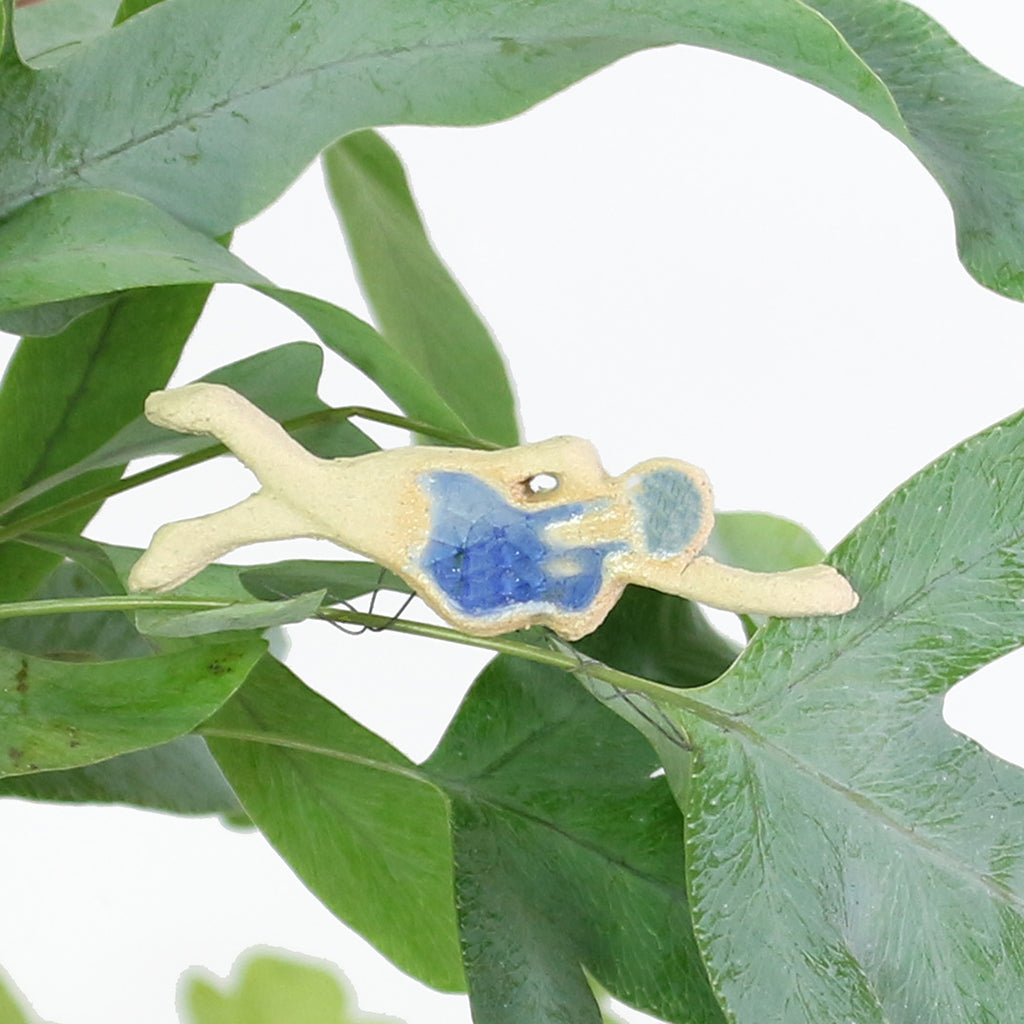 small ceramic and glass swimmer with dark blue cap and costume, with thin wire wrapped around house plant stem