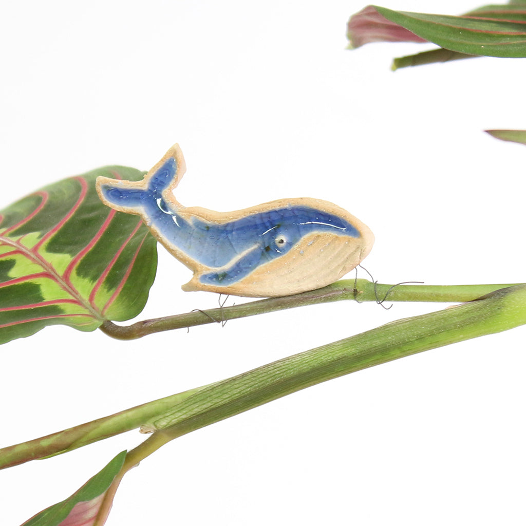 small ceramic and glass dark blue whale plant decoration, with thin wire wrapped around house plant stem